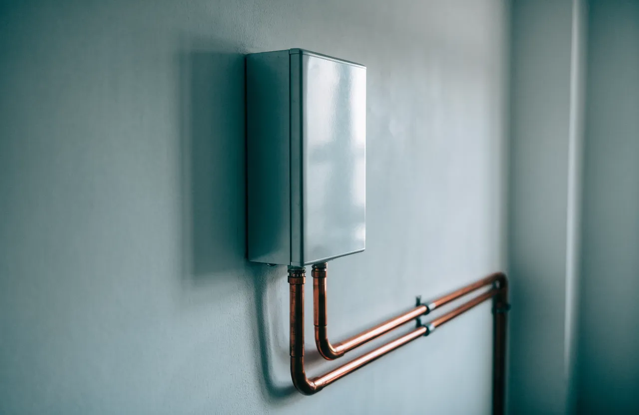 Compact wall-mounted tankless water heater with copper supply and outlet pipes running beneath it