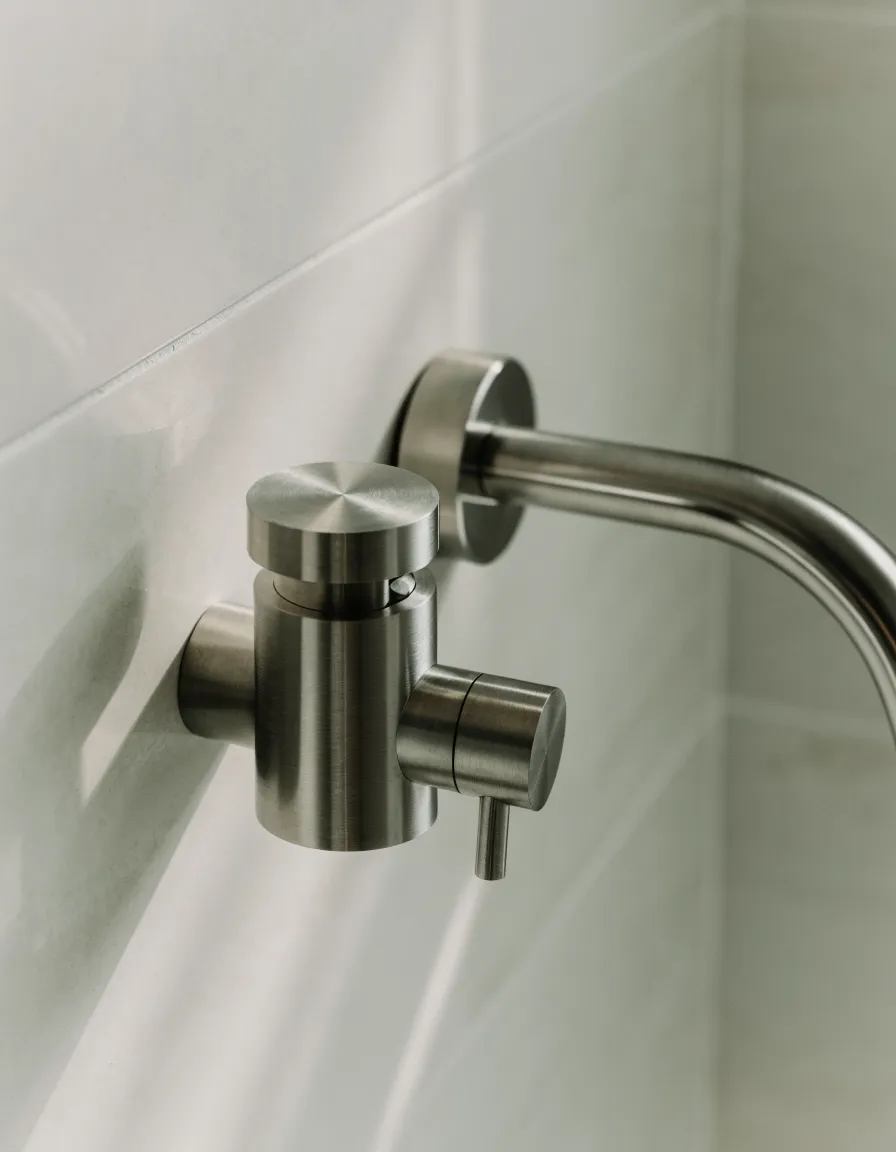 Brushed nickel shower valve trim and round shower arm on pale matte tile